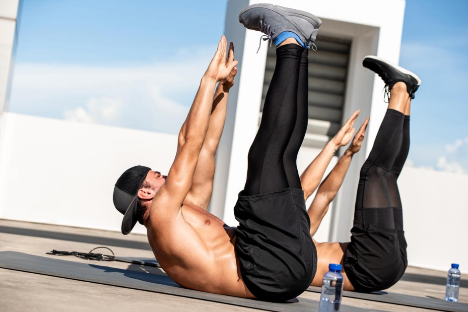 Deux hommes réalisant un exercice abdominal toe touch à l’extérieur d’une salle de sport